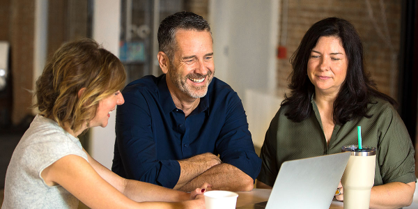 3 employees sitting and looking at computer, happily