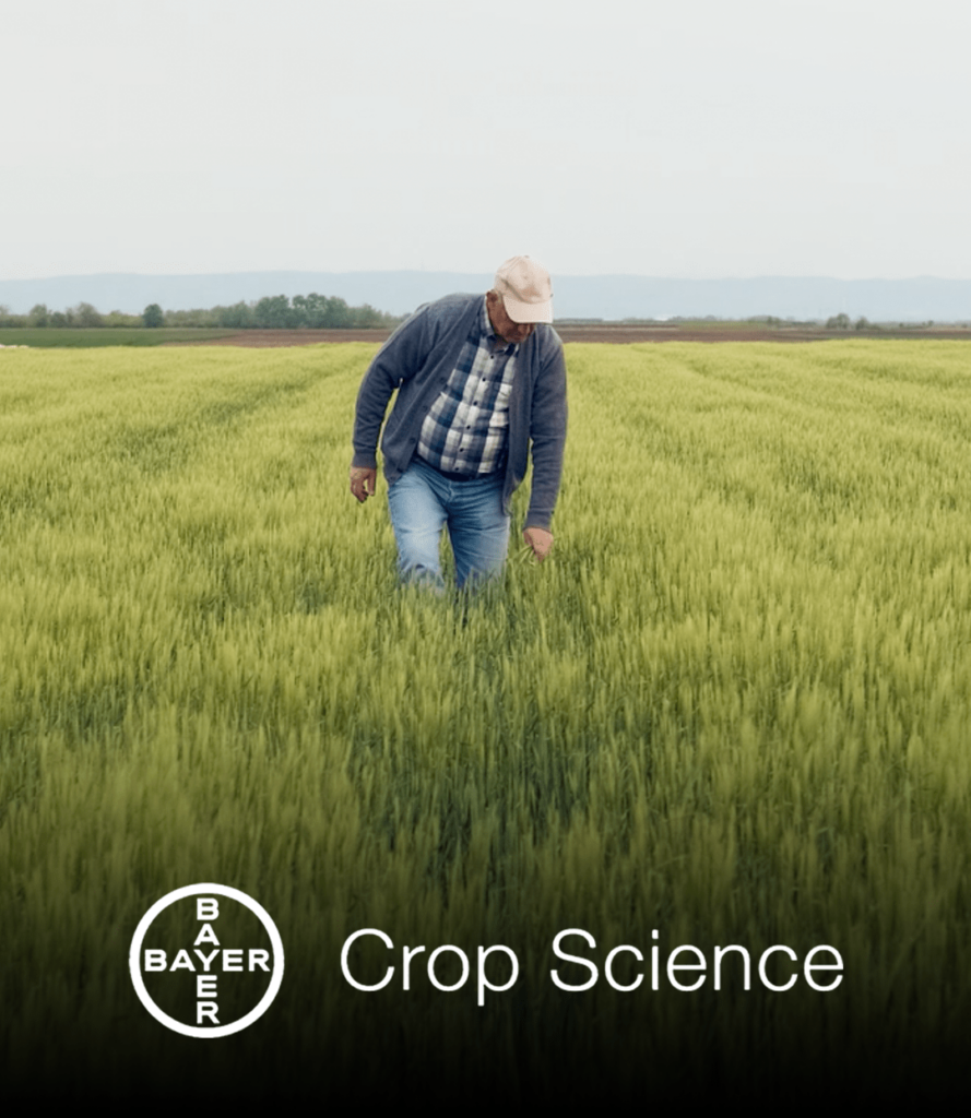 farmer walking through grass with Bayer Crop Science logo