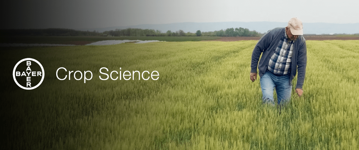 farmer walking through grass with Bayer Crop Science logo